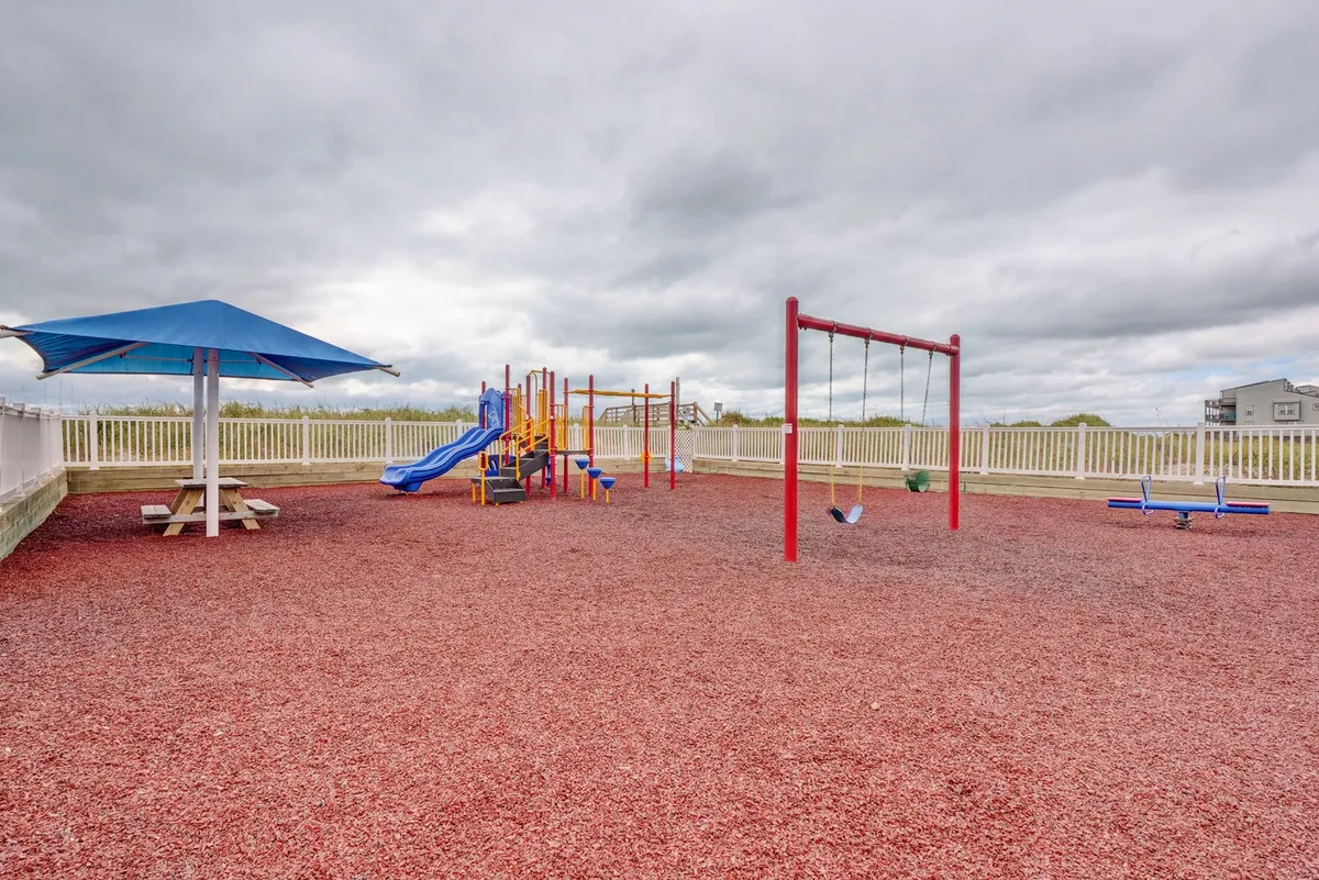 A cheerful outdoor playground featuring swings, playground equipment, a shaded picnic area, and surrounding greenery. Children play while parents relax nearby, capturing the essence of communal family enjoyment.