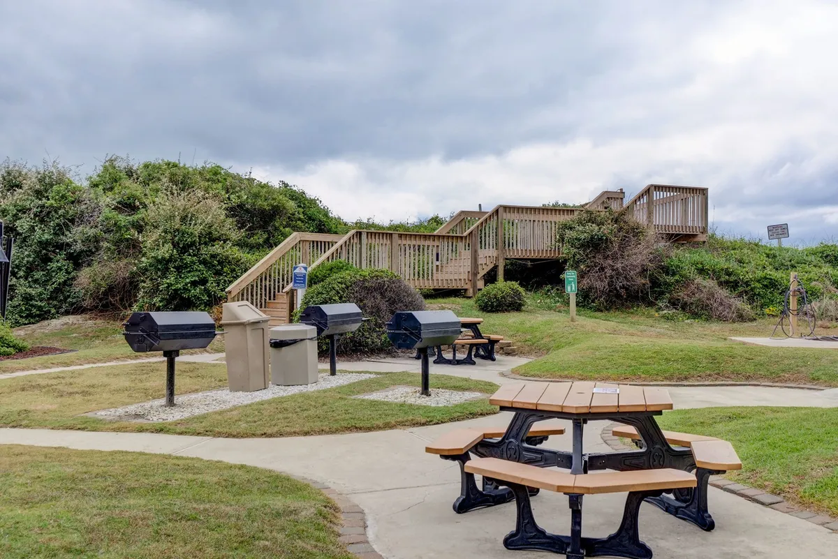 An inviting outdoor grilling and picnic area with barbecue grills, picnic tables, and stairs leading to a deck, set up for relaxed social gatherings and family meals.