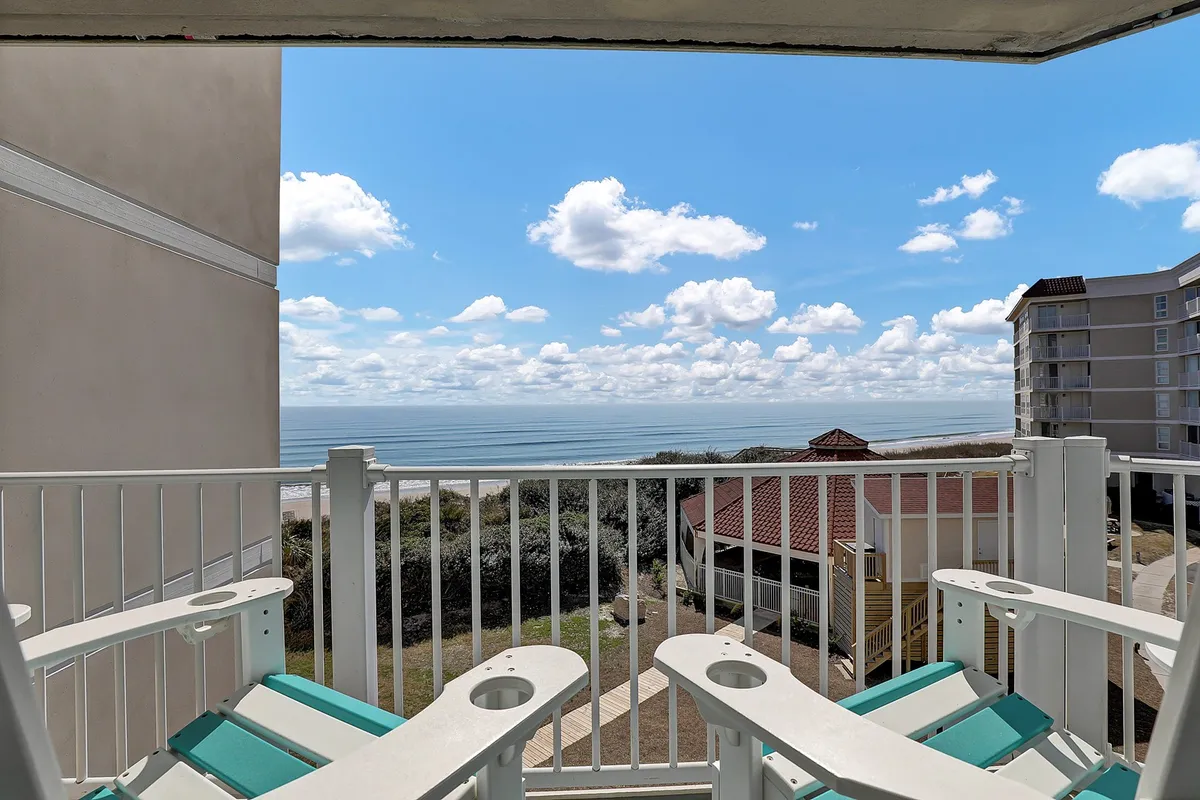 A serene oceanfront balcony with comfortable chairs overlooking gentle waves and soft clouds, offering a tranquil spot to savor sunrise coffee or unwind after a day of activities.