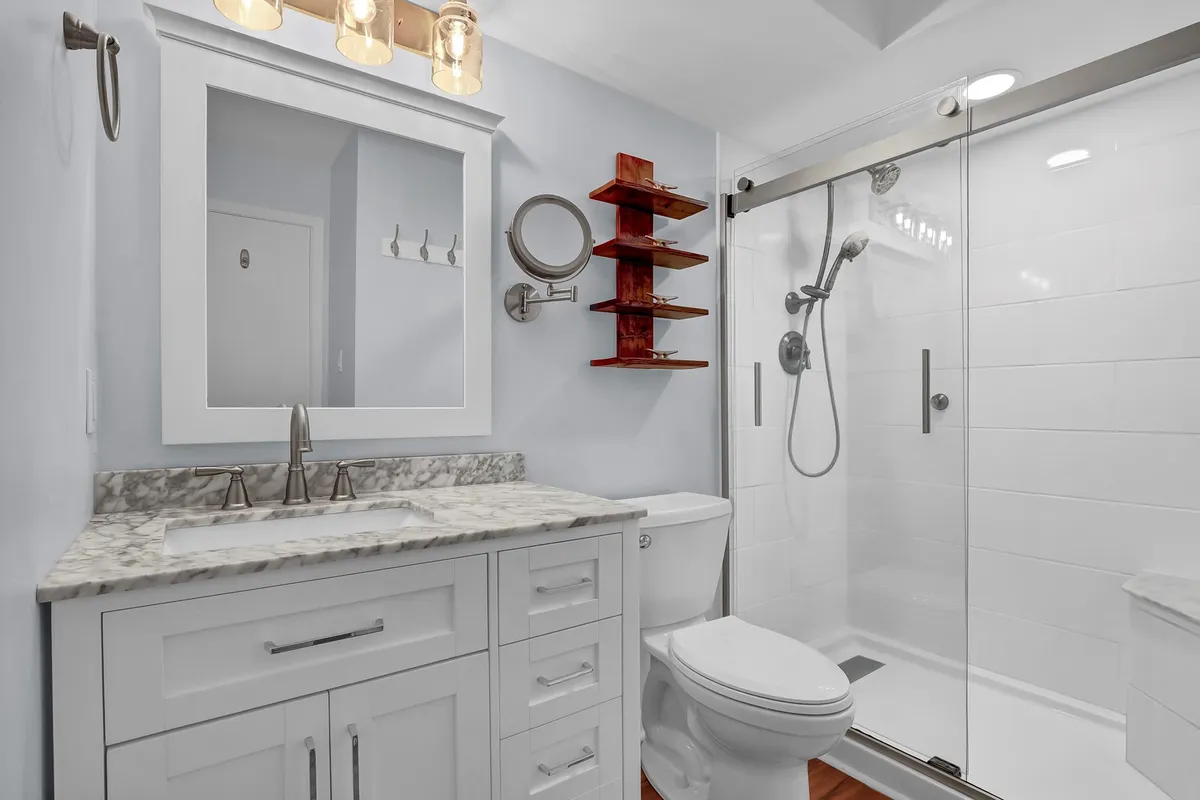 A modern, spa-like bathroom with a marble-topped vanity, glass shower enclosure, and contemporary lighting fixtures. The setting is immaculate, inviting, and visually refreshing, with details that elevate the sense of comfort and privacy.