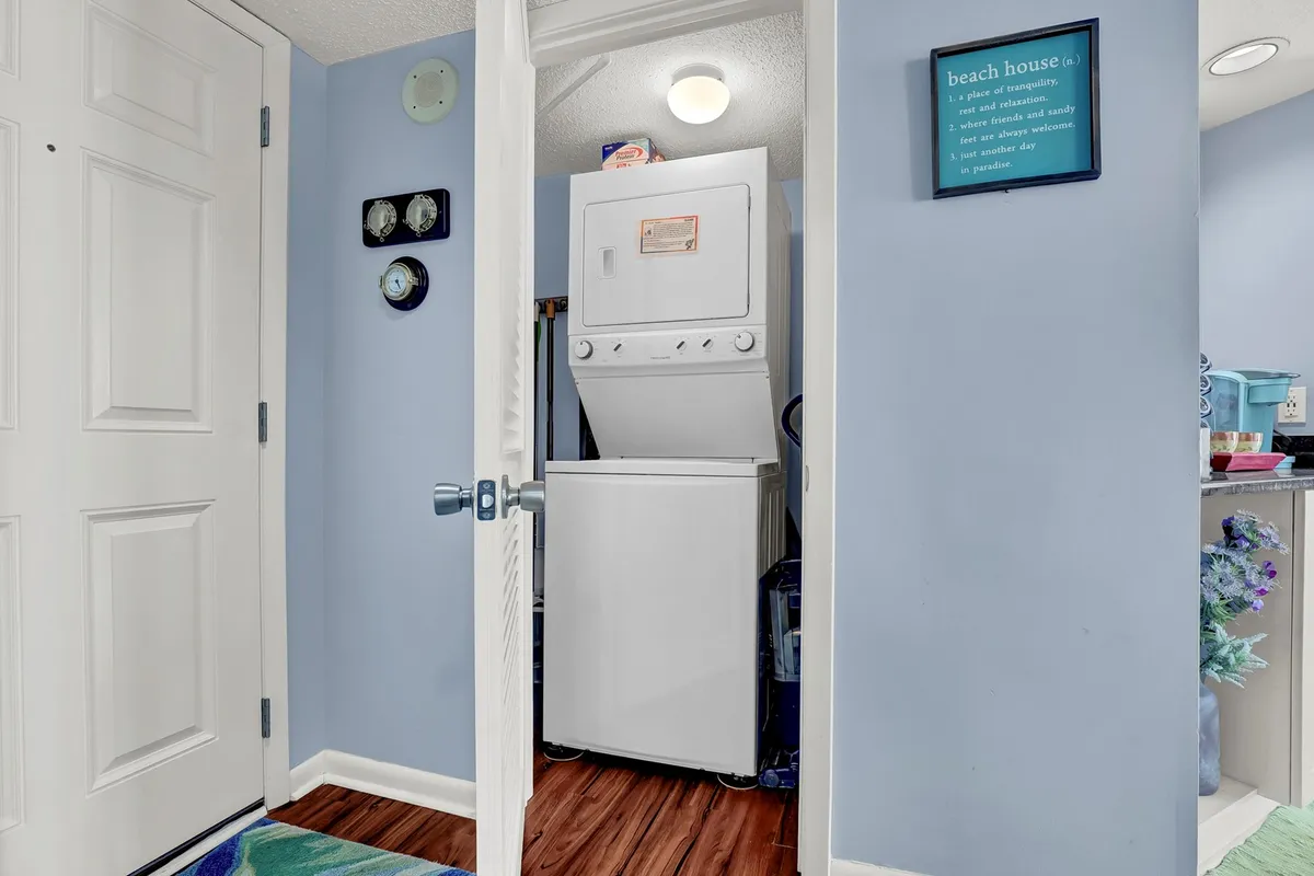A functional laundry area featuring a washing machine, a doorway with a decorative sign, and welcoming touches that make doing laundry feel effortless and convenient.