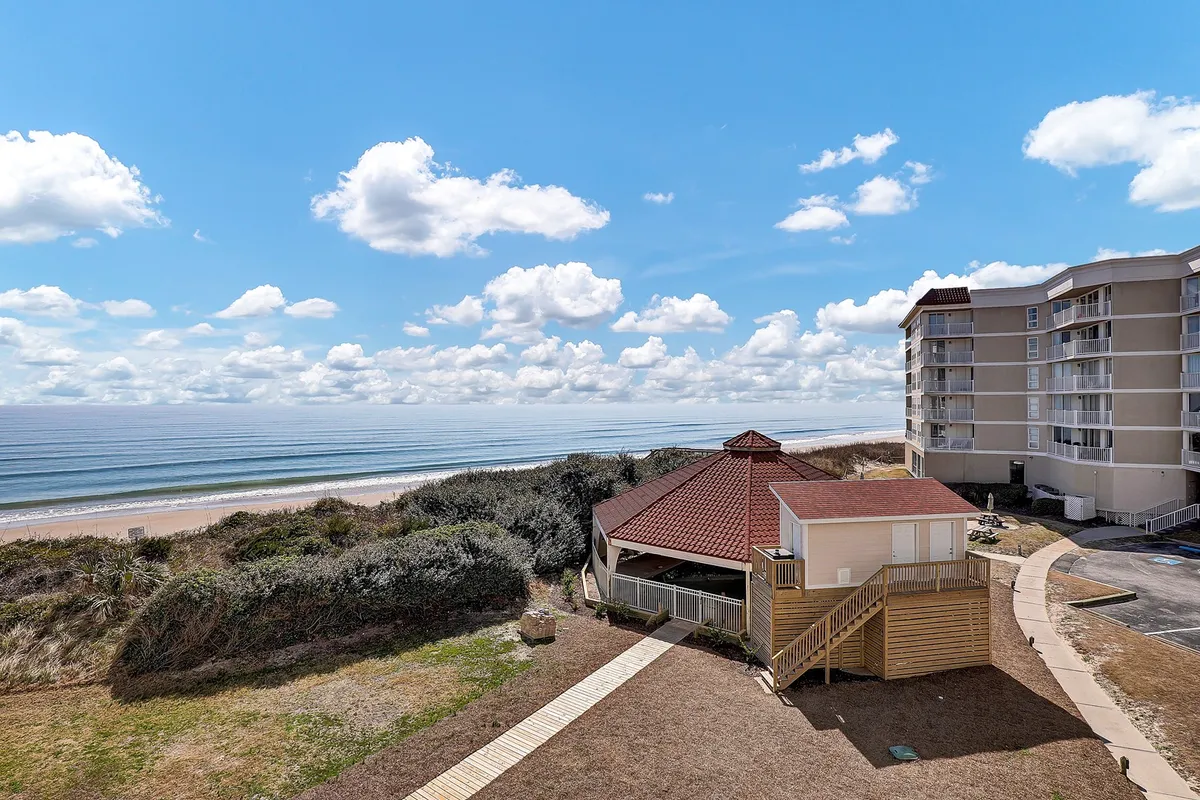The hero image showcases a charming beachfront gazebo overlooking gentle ocean waves, with a beautiful sky above and the condo building nearby. The tranquil setting suggests idyllic sunset gatherings, peaceful beach walks, and a front-row seat to North Topsail Beach's natural beauty.