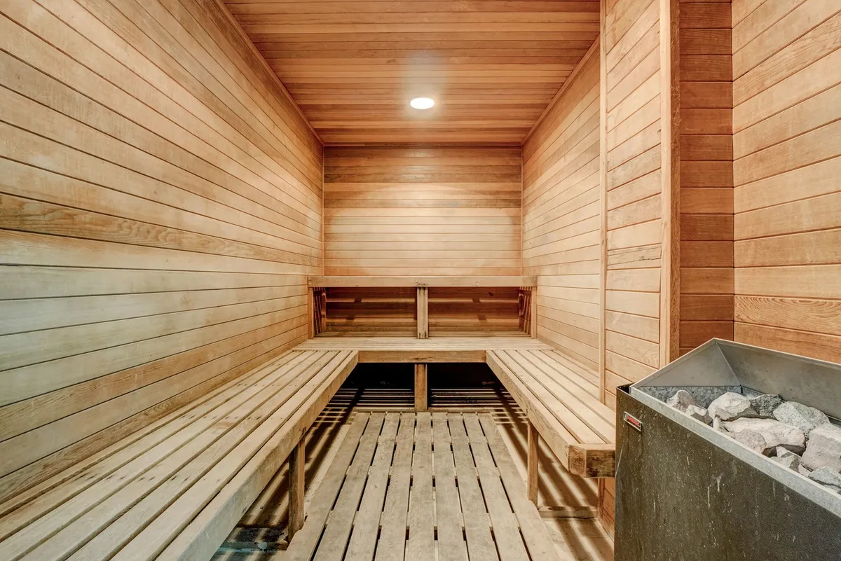 A serene sauna with wooden benches, a stone heater, and warm wood paneling. The tranquil ambiance is perfect for unwinding post-workout or enjoying a peaceful wellness routine.